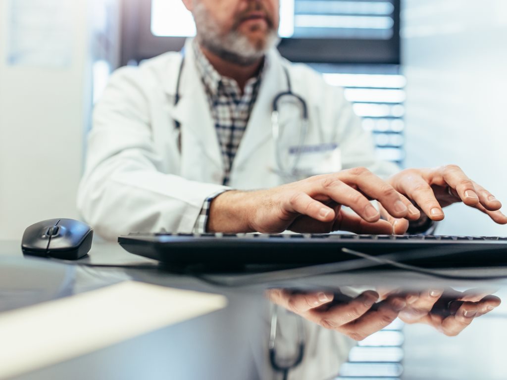 Closeup of hands of male doctor typing on computer keyboard.